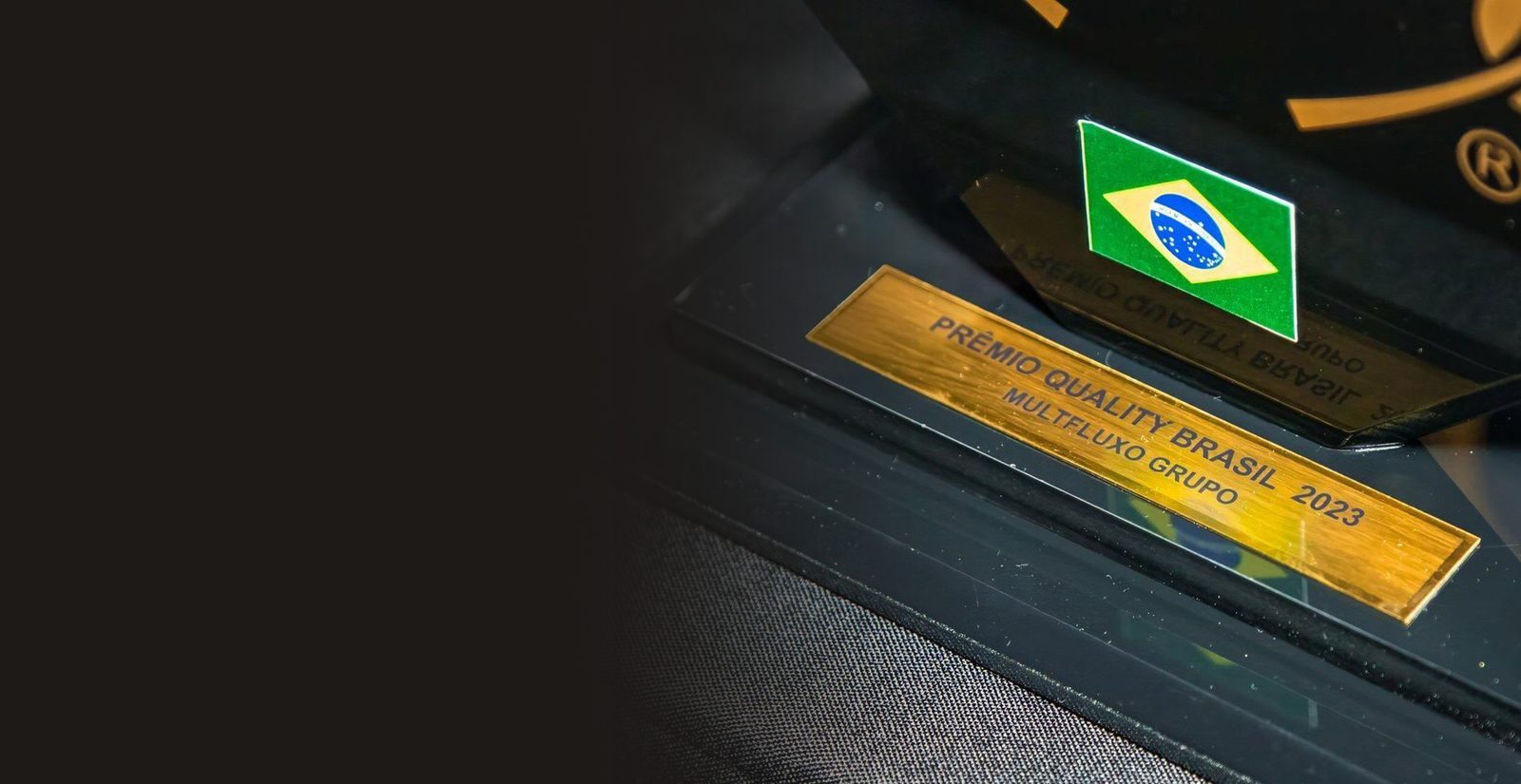 Placa dourada com a inscrição Prêmio Quality Brasil 2023, Multfluxo Grupo, e a bandeira do Brasil na base do troféu